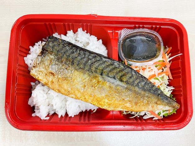 Pescado saba a la parrilla con salsa teriyaki en un tazón de arroz cubierto en el recipiente de plástico