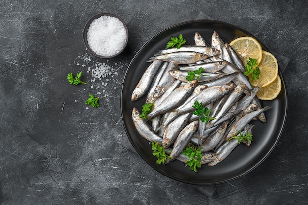 Pescado salado con limón y perejil sobre un fondo oscuro con espacio para copiar. Sardinas, pescado de mar.