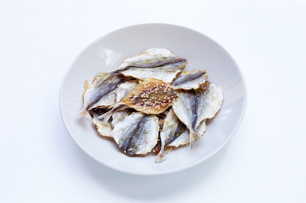 Pescado seco con semillas de sésamo en plato blanco sobre fondo blanco.