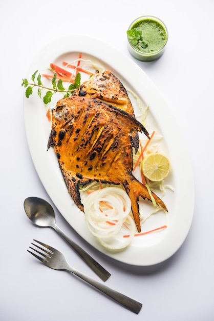 Pescado Tandoori Pomfret cocido en horno de barro y aderezado con ensalada de limón, menta, repollo y zanahoria. Enfoque selectivo