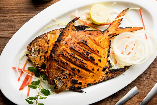 Pescado Tandoori Pomfret cocido en horno de barro y aderezado con ensalada de limón, menta, repollo y zanahoria. Enfoque selectivo