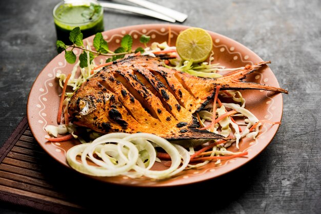 Pescado Tandoori Pomfret cocido en horno de barro y aderezado con ensalada de limón, menta, repollo y zanahoria. Enfoque selectivo