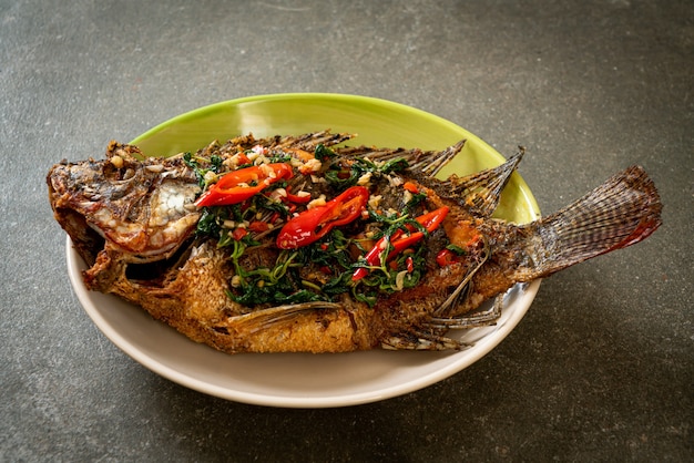 Pescado tilapia frito con salsa de ajo y albahaca en la parte superior - estilo de comida casera