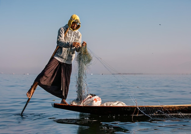 Pescador asiático tradicional con una red de pesca en un barco en el lago  inle myanmar birmania