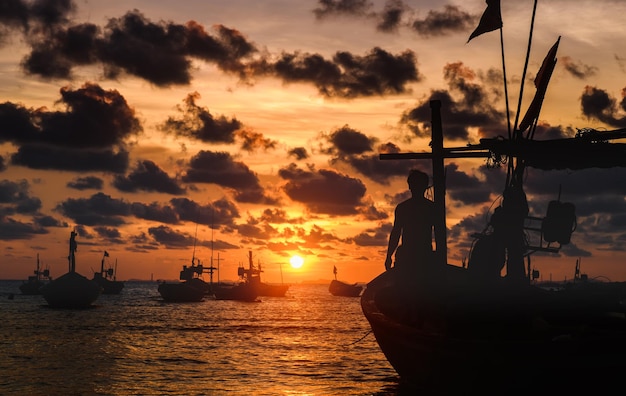 Pescador y barco de madera en la orilla del mar con la hora del atardecer iluminación cálida oscura
