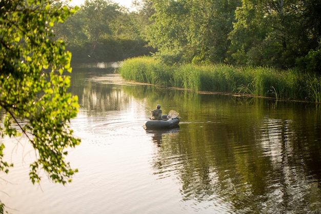 Un pescador en un bote flota en el río y pesca.