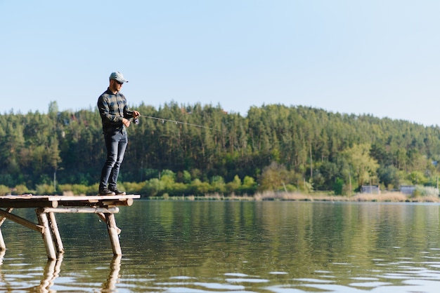 Pescador con caña, carrete giratorio en la orilla del río