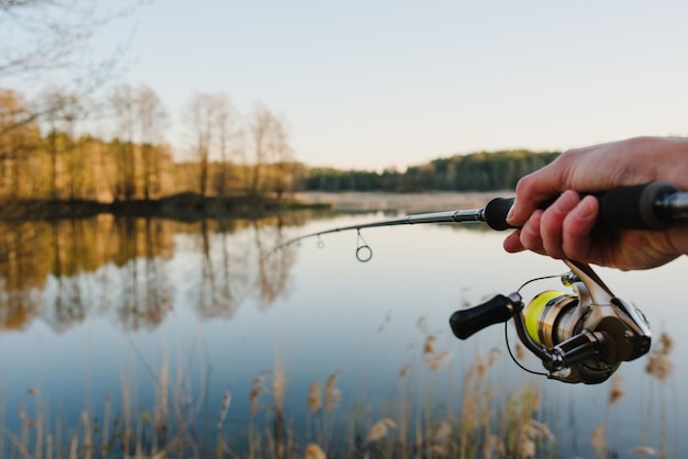 Un pescador con una caña de pescar en la mano atrapa un pez en la orilla de un lago o río Día de pesca Girando en la mano sobre el fondo del estanque