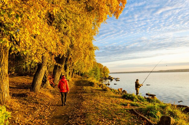 Un pescador con una caña de pescar en la orilla del lago en otoño.