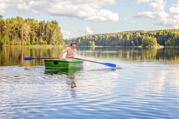 Pescador con cañas de pescar está pescando en un bote de madera en el lago o río