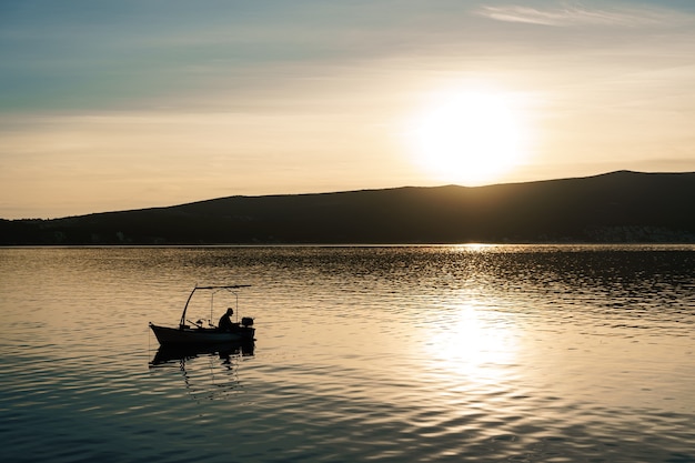 Un pescador captura peces en el mar con el telón de fondo de una montaña y una puesta de sol.