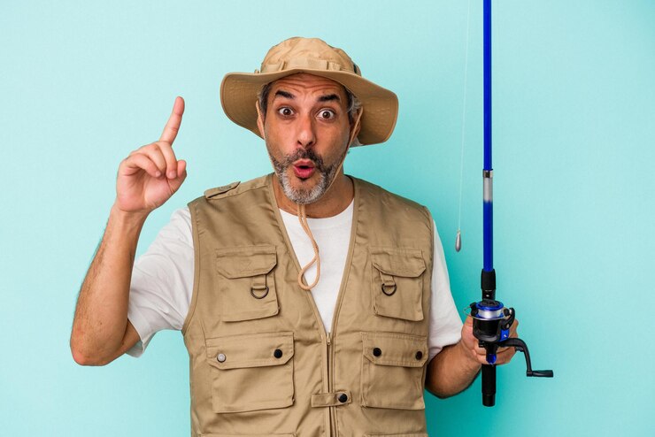 Foto pescador caucásico de mediana edad sosteniendo una caña aislada de fondo azul con un concepto de inspiración de ideas
