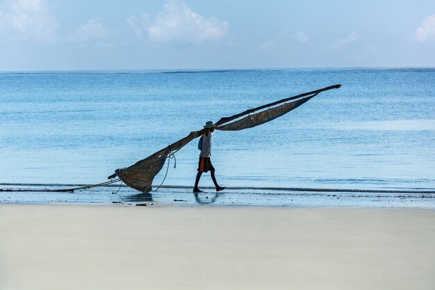 Pescador da áfrica mombaça caminhando na praia com uma vela para um barco,