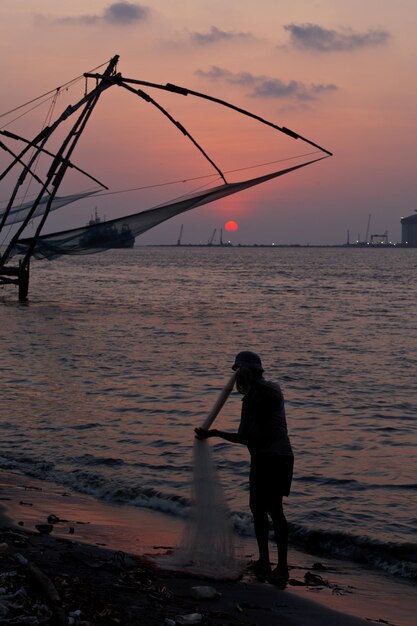 Pescador e redes de pesca chinesas no pôr do sol Kochi Kerala Índia