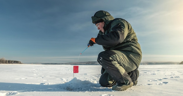 Pescador está pescando em um buraco em um grande lago congelado em um dia ensolarado A alegria da pesca de inverno