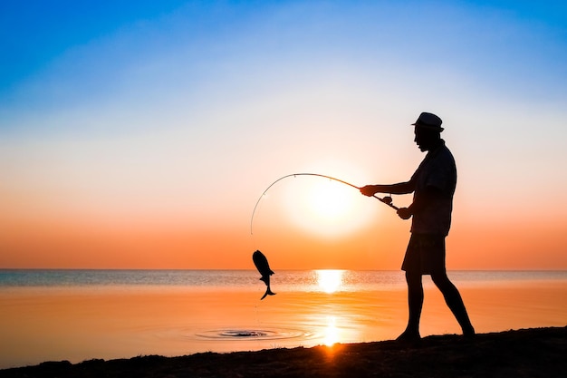 Un pescador feliz pescando peces junto al mar en viajes de silueta de naturaleza