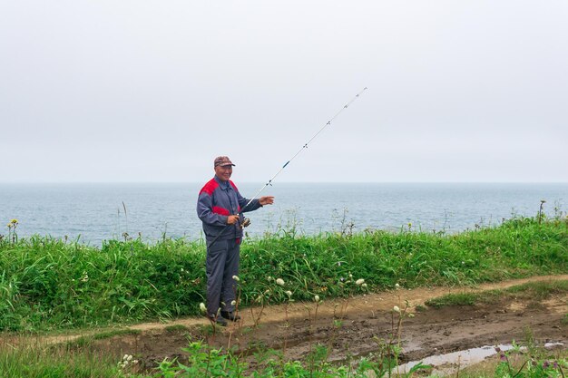 Pescador idoso verifica sua vara de pescar à beira-mar
