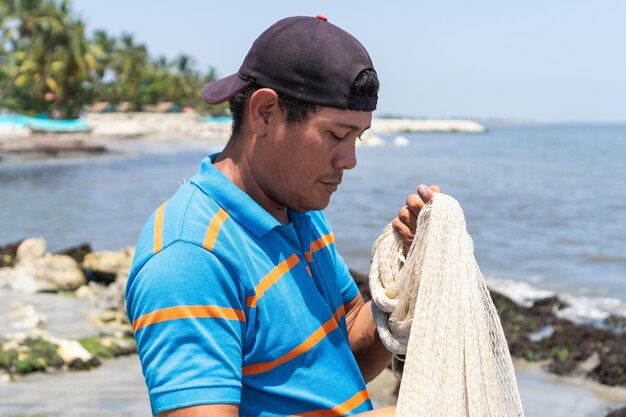 Pescador latino en la playa reparando su red de pesca