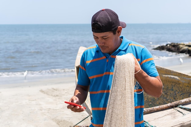 Pescador latino revisando su celular en la playa