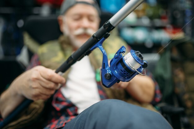 Pescador masculino con caña sentado en una silla, tienda de pesca.