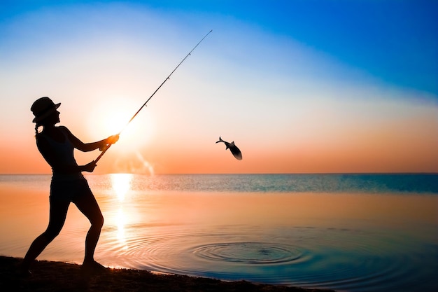 Un pescador de niña feliz captura peces junto al mar en viajes de silueta de naturaleza