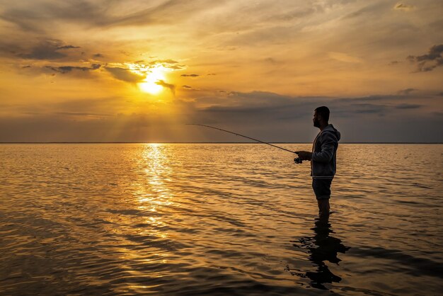 Pescador parado en el agua al hermoso atardecer