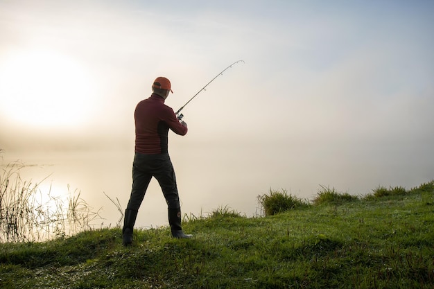 Pescador pega peixe girando vara no lago ao nascer do sol