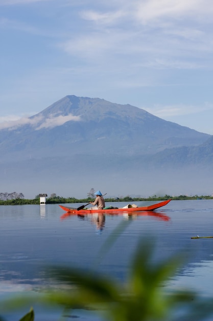 Un pescador pesca con una canoa de madera en Rawa Pening con el monte Merbabu al fondo Canoa de madera