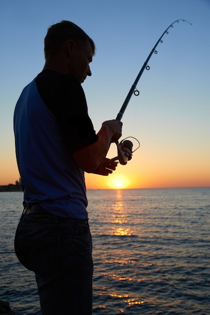 Pescador pescando na silhueta do lago ao pôr do sol