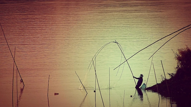 Foto pescador pescando en el río durante la puesta de sol