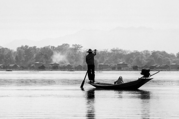 Pescador de pie en un barco en el lago contra el cielo