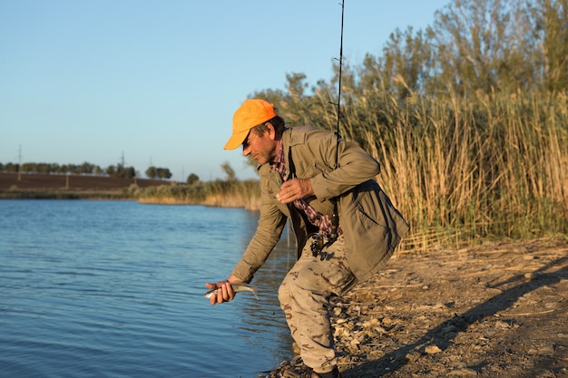 Pescador de pie en la orilla del río y tratando de pescar un pez. Deporte, recreación, estilo de vida.