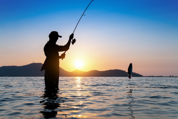 Pescador que joga sua haste, pescando no lago, cena bonita do por do sol da manhã.