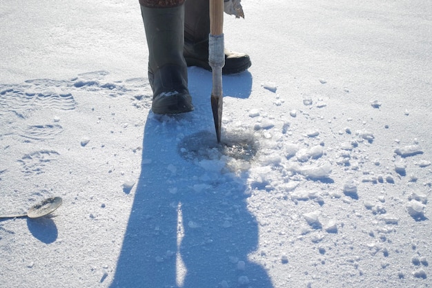 Pescador rompe un agujero en el río invierno pesca en hielo pesca en hielo en invierno pequeña caña de pescar stan