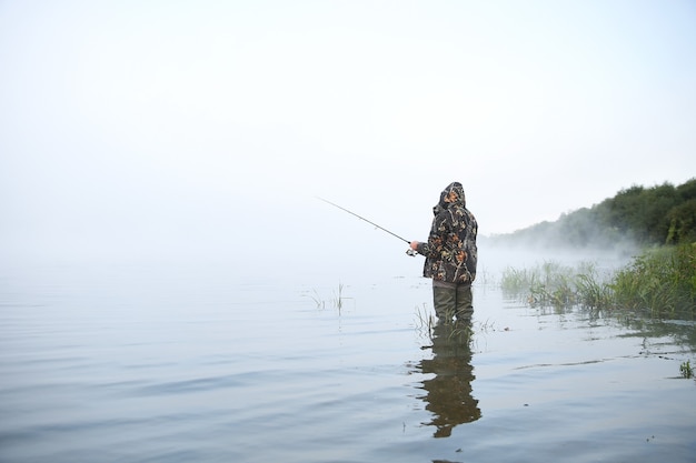 Pescador segurando vara de pescar no lago em meio à névoa
