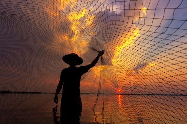 Foto pescador de silueta con puesta de sol