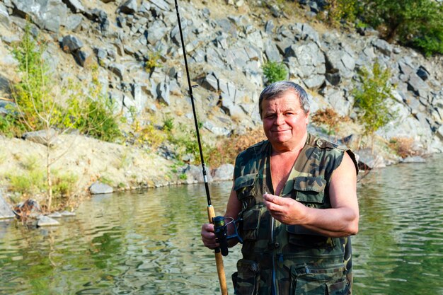 Pescador sonriente con una caña de pescar en un lago de montaña