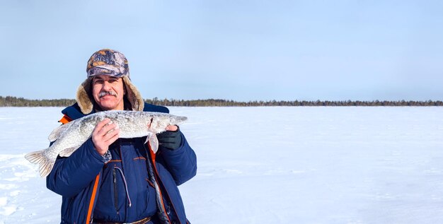 El pescador sostiene con orgullo una gran pica contra el sereno telón de fondo de un paisaje cubierto de nieve.