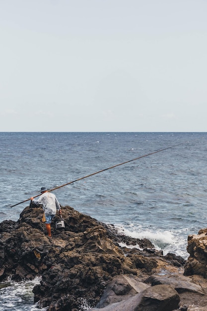 Pescador yendo a las rocas con su caña de pescar y equipo