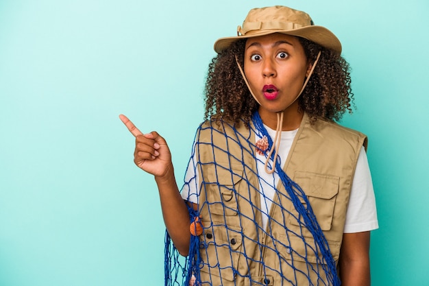 Pescadora afroamericana joven sosteniendo net aislado sobre fondo azul apuntando hacia el lado