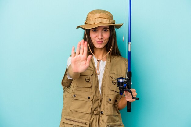 Foto pescadora caucásica joven aislada en el fondo azul que se coloca con la mano extendida que muestra la señal de pare, previniéndole.