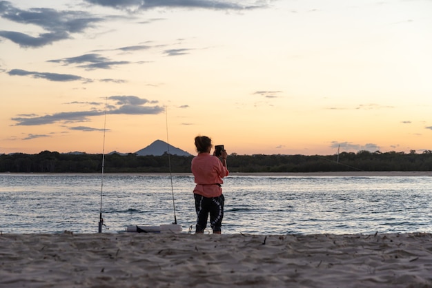 Pescadora tomada una foto al atardecer en una playa. Concepto de estilo de vida