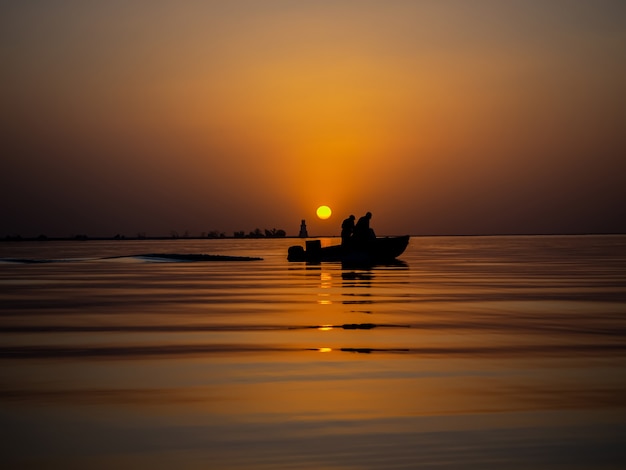 Pescadores en un barco de pesca de una puesta de sol dorada en el mar.