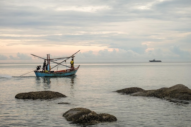 Pescadores navegando en barco en el mar contra un cielo nublado durante la puesta de sol