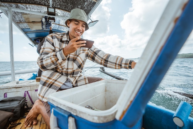 Pescadores tiram fotos do conteúdo de uma caixa de peixe com uma câmera de telefone celular em um pequeno barco de pesca