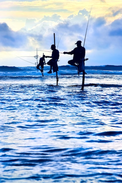 Pescadores tradicionales en palos al atardecer en Sri Lanka Imagen del paisaje marino en colores azul y amarillo