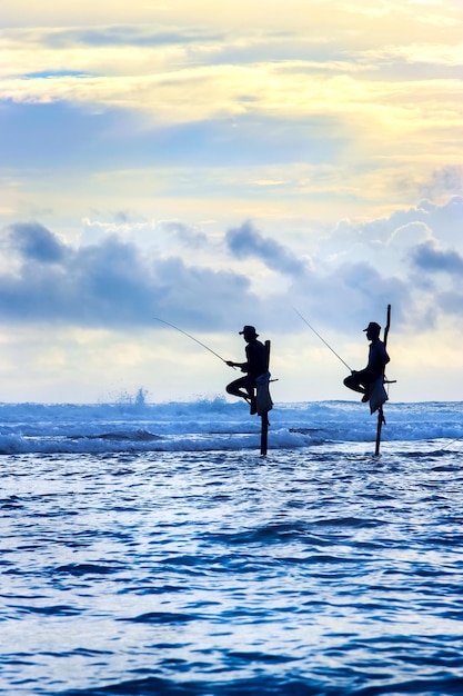 Pescadores tradicionales en palos al atardecer en Sri Lanka Imagen del paisaje marino en colores azul y amarillo