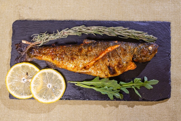 Pescados dorados asados con limón, hierbas, sal sobre fondo negro. Concepto de comida sana. Marco de comida.