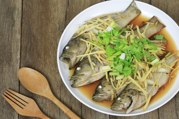 Los pescados del mero azul cocieron al vapor de la salsa de soja en el plato blanco en piso de madera marrón.