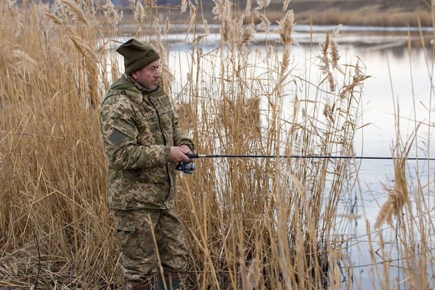 Pescar nos juncos para girar em águas tranquilas Um homem com roupas de camuflagem em clima frio
